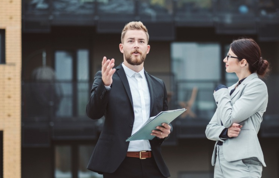 agent wearing black suit talking to woman in gray sauit